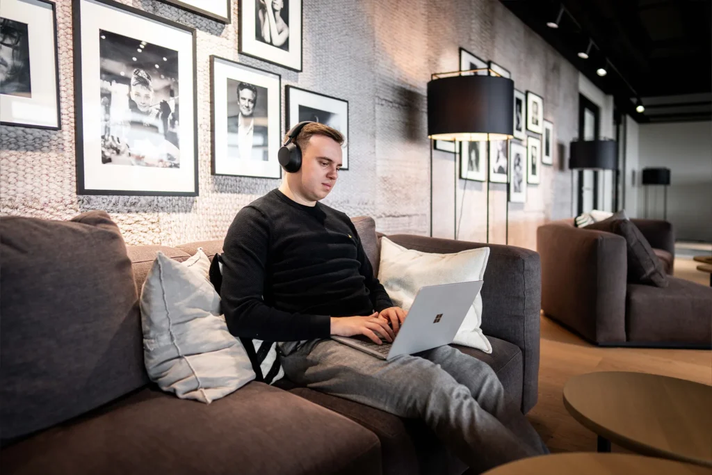 Eine Person sitzt auf einem Sofa und führt mit einem Laptop ein Meeting – zeigt die Flexibilität und Effizienz der Meeting App von CoffeeNet 365.