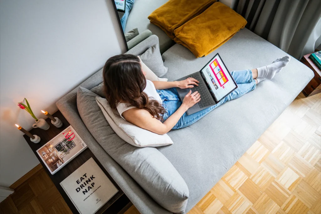 Frau sitzt mit ihrem Laptop auf dem Sofa und arbeitet von Zhause